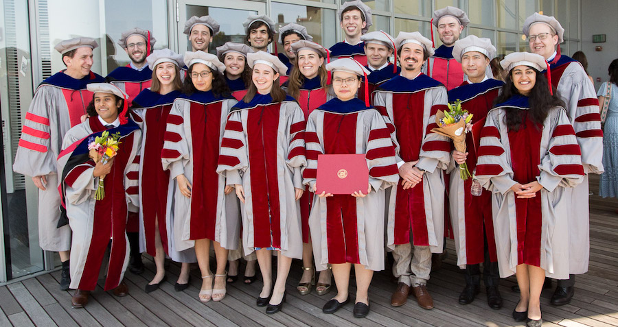 Image of graduates smiling in their regalia and posing for the camera