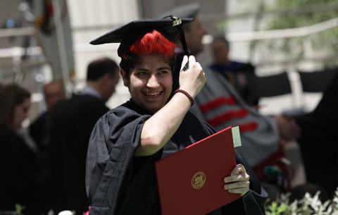 Female student adjusts her tassle with diploma in hand