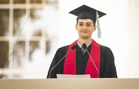 Photo of Adam Joseph Miller at the podium delivering the salute from the graduate students