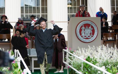 Image of a graduate happily crossing the stage after receiving his scroll