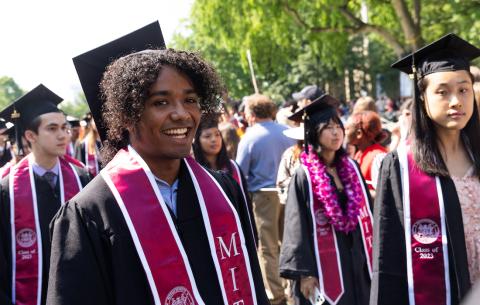 Image of graduates walking in the graduate division of the academic procession. The graduates are smiling as they make their way into Killian Court. 