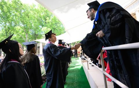 Image of graduate shaking the hands of a faculty member on stage before they receive their diploma