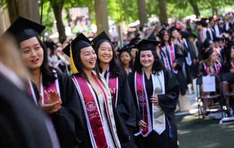 Image of graduates smiling and waiting to cross the stage to receive their diploma