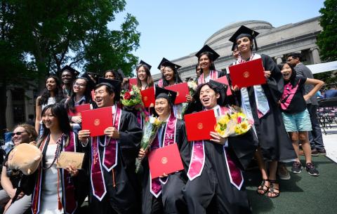 Image of a group of graduates holding their diplomas and smiling for a group photo