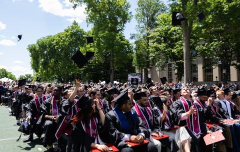 Image of the graduates in the audience smiling and throwing their caps in the air