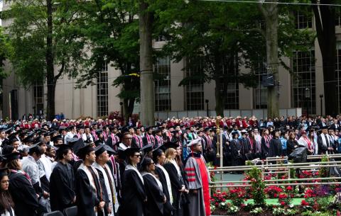 Image of the graduates in the audience standing and looking towards the Commencement stage